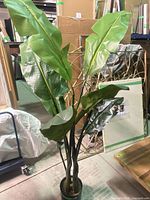 Full view of faux tropical palm leaf tree standing in black plastic pot