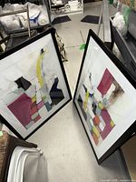 Both framed prints standing on floor, show black frames and abstract designs