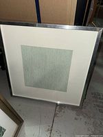 Framed square artwork showing green textured wallpaper sample in metal frame