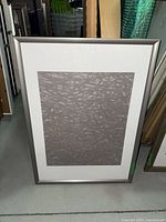 Framed abstract wallpaper art standing on floor with other frames visible behind