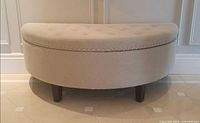 Front view of beige half-moon ottoman showing nailhead trim and legs