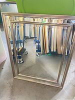 Front view of rectangular champagne framed mirror leaning against wall