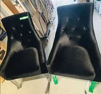Pair of black velvet dining chairs showing seats, tufted backs, acrylic legs