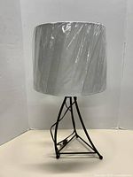 Full view of lamp with shade wrapped in plastic on neutral backdrop