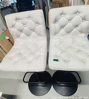 Front view of both beige linen tufted stools on black bases