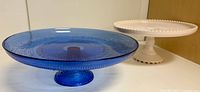 Blue beaded glass cake stand and pink milk glass pedestal cake stand side by side