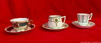 Three porcelain cup and saucer sets arranged side by side on red background