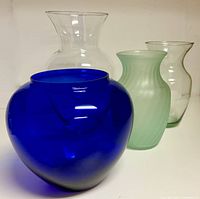 Four vases grouped: cobalt blue round, frosted green cylindrical, tall clear flared, medium clear tapered