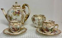 Full view of teapot, sugar bowl, two demitasse cups with saucers showing pattern and gilt detail