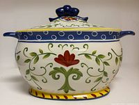 front view of ceramic soup tureen with lid showing floral decoration, handles, finial, and base