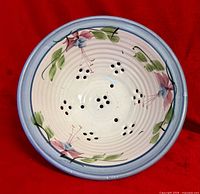 Top view showing hand-painted floral design, blue rim and drainage holes of the ceramic berry bowl