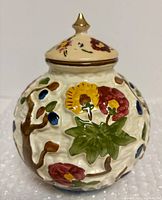 Full view of spherical earthenware vase with lid showing raised-relief Indian Tree floral design and finial