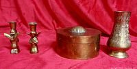 Lot overview showing brass box, two angel candle holders, etched vase against red backdrop