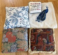 All four throw pillows and separate peacock pillow cover laid out on floor
