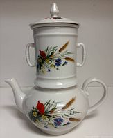 Stacked view showing teapot base, cylindrical mug/strainer and lid with floral motif