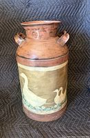 Full view of painted metal milk can showing faux-bronze finish, handles, and goose motif band