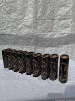 Eight matching black ceramic vases with gold swirl design lined side by side