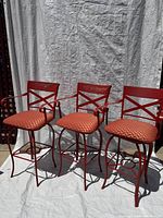 three orange wrought iron bar stools with cushions, full view