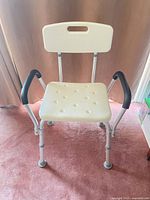 Front view of adjustable bath/shower chair showing seat perforations, padded armrests, rubber feet