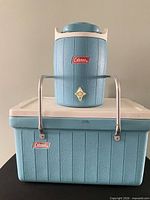 Front view of cooler with water jug stacked on top, showing color, logos, handles and spigots