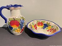 Pitcher and bowl front view showing hand-painted fruit motif, blue trim