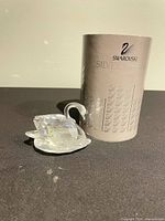Crystal goose figurine beside original cylindrical box