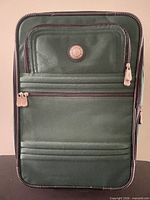 Front view of dark green Traveler's Club carry-on with external zip pockets and brand emblem
