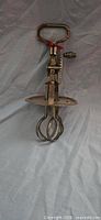 Full view of antique metal hand mixer showing crank, beaters and splatter guard