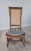Front view of rocking chair showing cane back and needlepoint cushion
