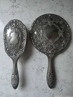 front view of silver-plated hand mirror and hair brush showing ornate design