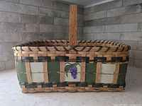 Front view showing basket shape, handle, painted grape panel and green accent weavers