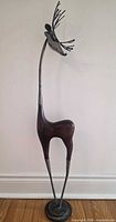 Full view of tall stylized deer sculpture showing metal base, long legs, wooden body and metal neck/head