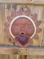 Full view terracotta sun face wall plaque hanging on wood fence