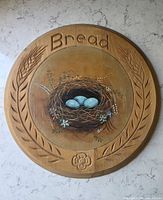 Full view of round wooden bread board showing carved border and painted nest