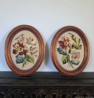 Both oval framed needlepoint artworks side by side