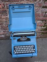 Typewriter open with lid upright showing keyboard, carriage and ribbon area