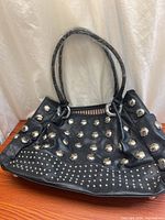 Front view of black vinyl handbag showing studs and handles