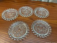 All five clear glass coasters displayed on wood surface showing rose design and hobnail rim