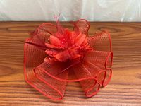 Front view of red fascinator showing mesh loops, flower, feathers and beads