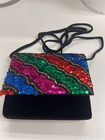 Front view showing multicolor sequined flap, black velvet body, braided strap