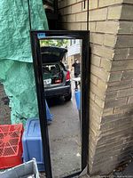 Frontal view of black framed door mirror leaning against wall