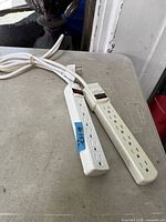 Two white 6-outlet power strips with cords and reset switches placed on table