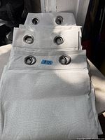 Stack of three folded light grey drapery panels with metal grommets