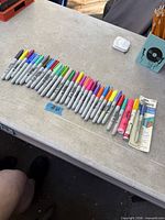 Row of assorted Sharpie markers arranged on table with sealed blister pack at right