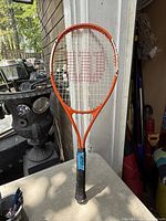 Full view of Wilson orange tennis racket standing upright