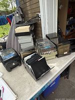 Overview of multiple plastic diskette cases, open tray of floppy disks and large black locking case on table