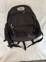 Front view of black PING Golf backpack showing logo, multiple pockets, shoulder straps