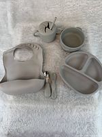 Entire six-piece grey silicone baby feeding set displayed on white fabric