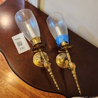 Two brass wall sconces with glass shades placed on table