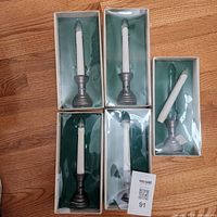 Five boxed battery-operated taper candles with holders, one candle partially removed for view